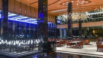 Eine moderne Hotelhalle mit Glasfassade, Marmorboden und einer zentralen Sitzecke mit Tischen und Stühlen.