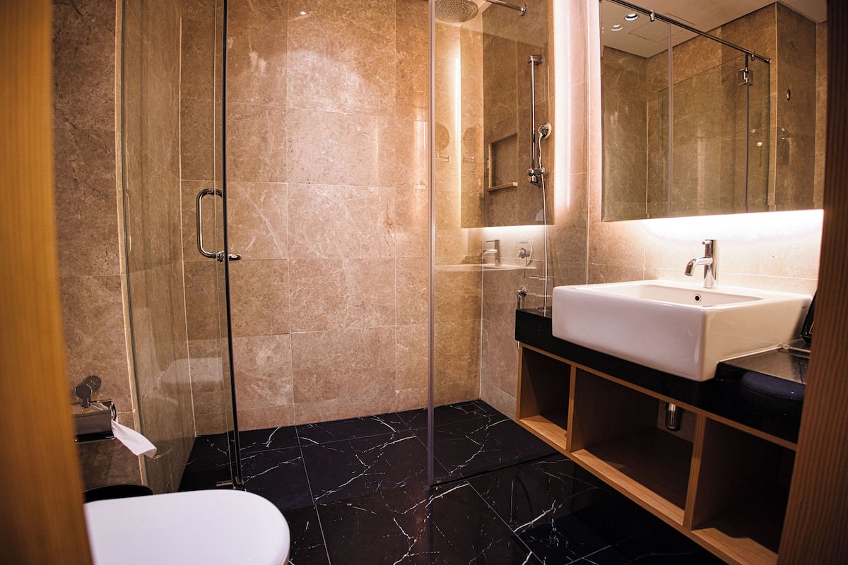 Une salle de bain moderne avec une douche à parois de verre, un lavabo blanc et un revêtement de sol en marbre.
