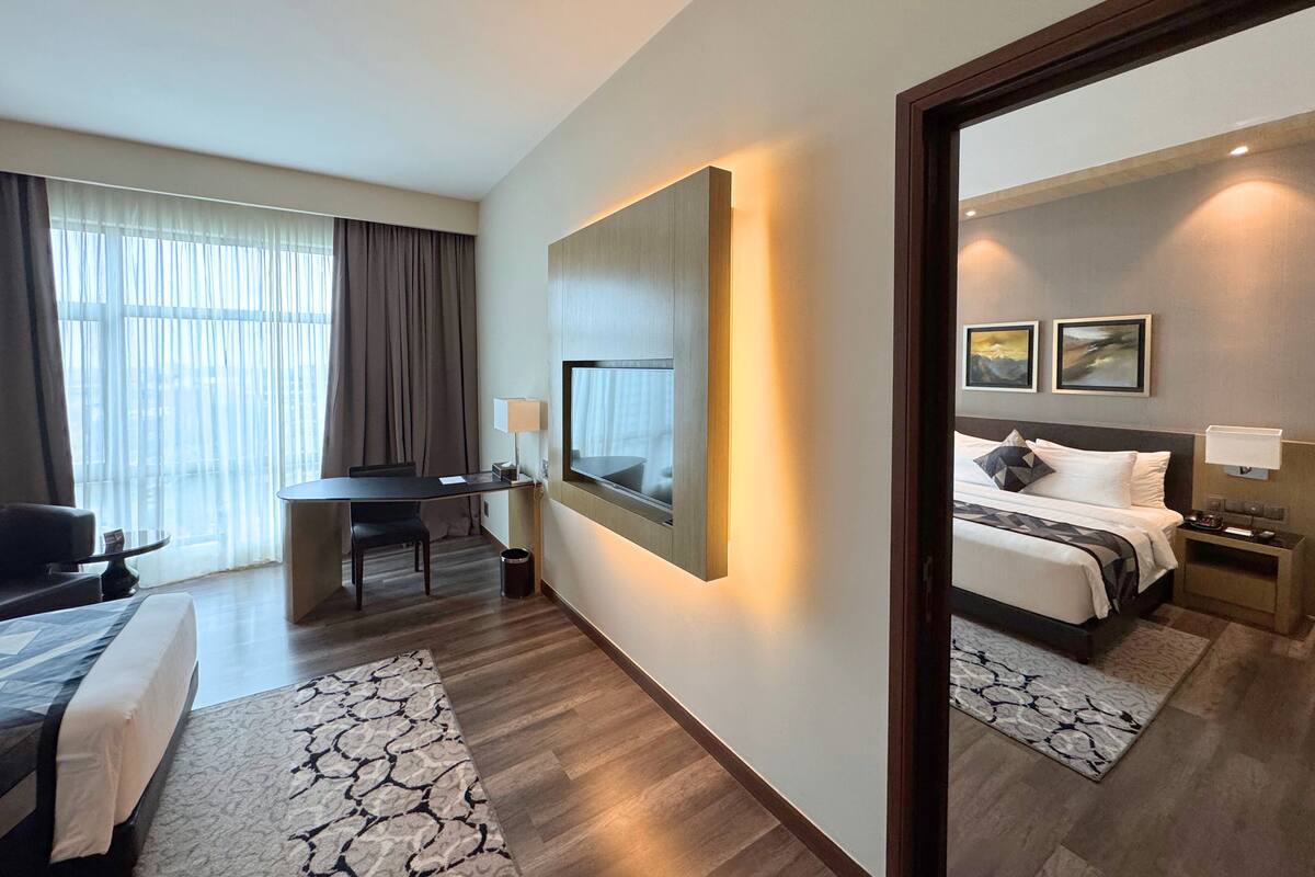 Une chambre d’hôtel avec un lit, un bureau, une chaise, un grand miroir et une vue sur la ville par la fenêtre.