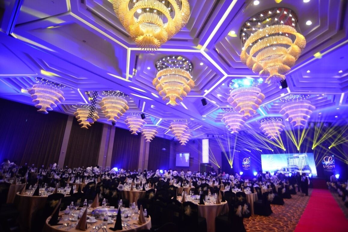 A banquet hall with multiple round tables set for a formal event, featuring a modern ceiling design with geometric patterns and large chandeliers.