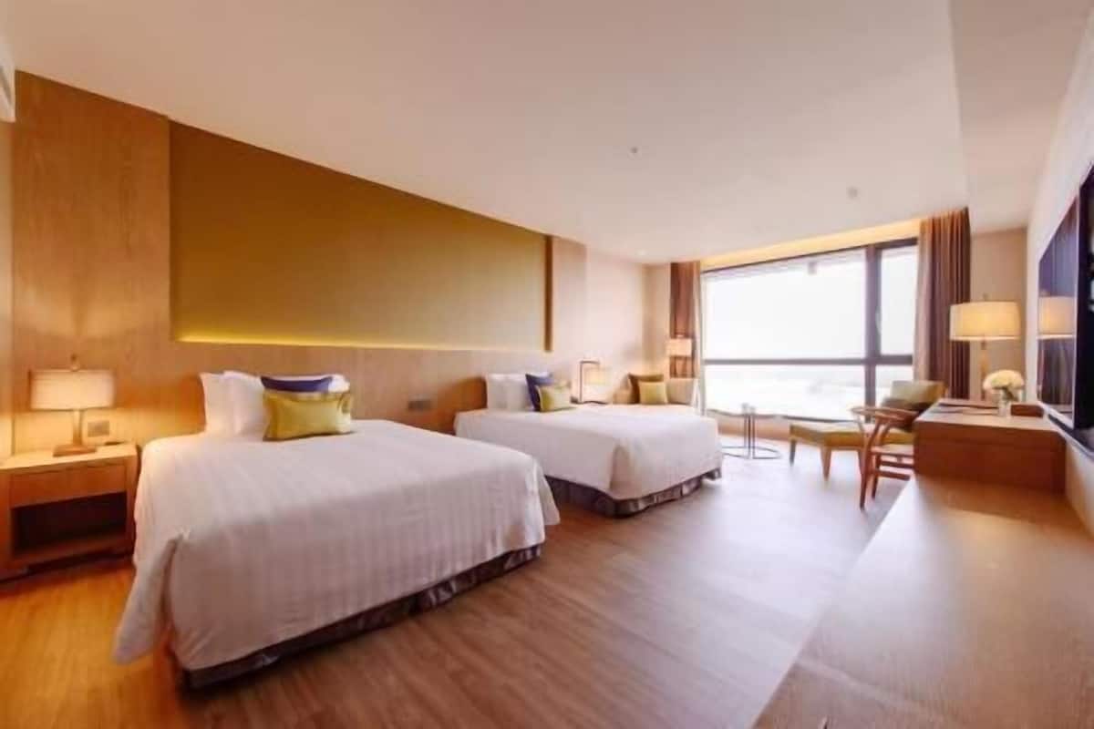 Habitación de hotel con dos camas, un escritorio, una silla y un ventanal grande.