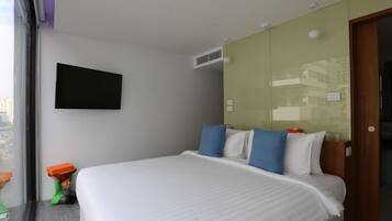 Habitación de hotel con cama, televisor montado, ventana con vista a la ciudad y una puerta.