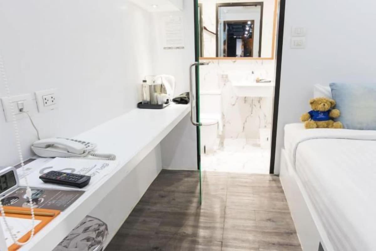 Ett hotellrum med ett skrivbord, en säng, en nallebjörn och en spegel.