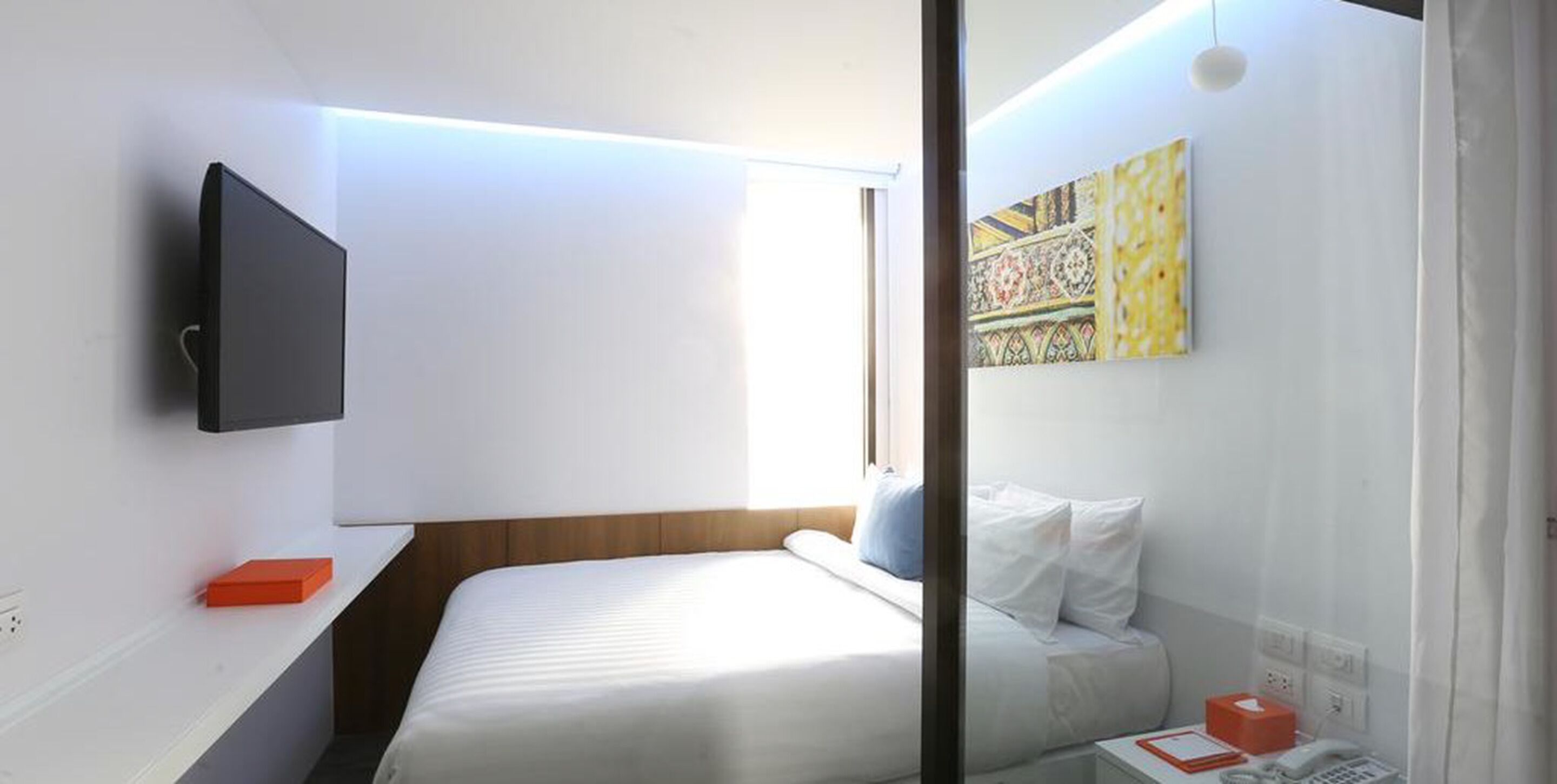 Ein Hotelzimmer mit Bett, Nachttisch, Wandfernseher und einem Fenster mit Vorhängen.