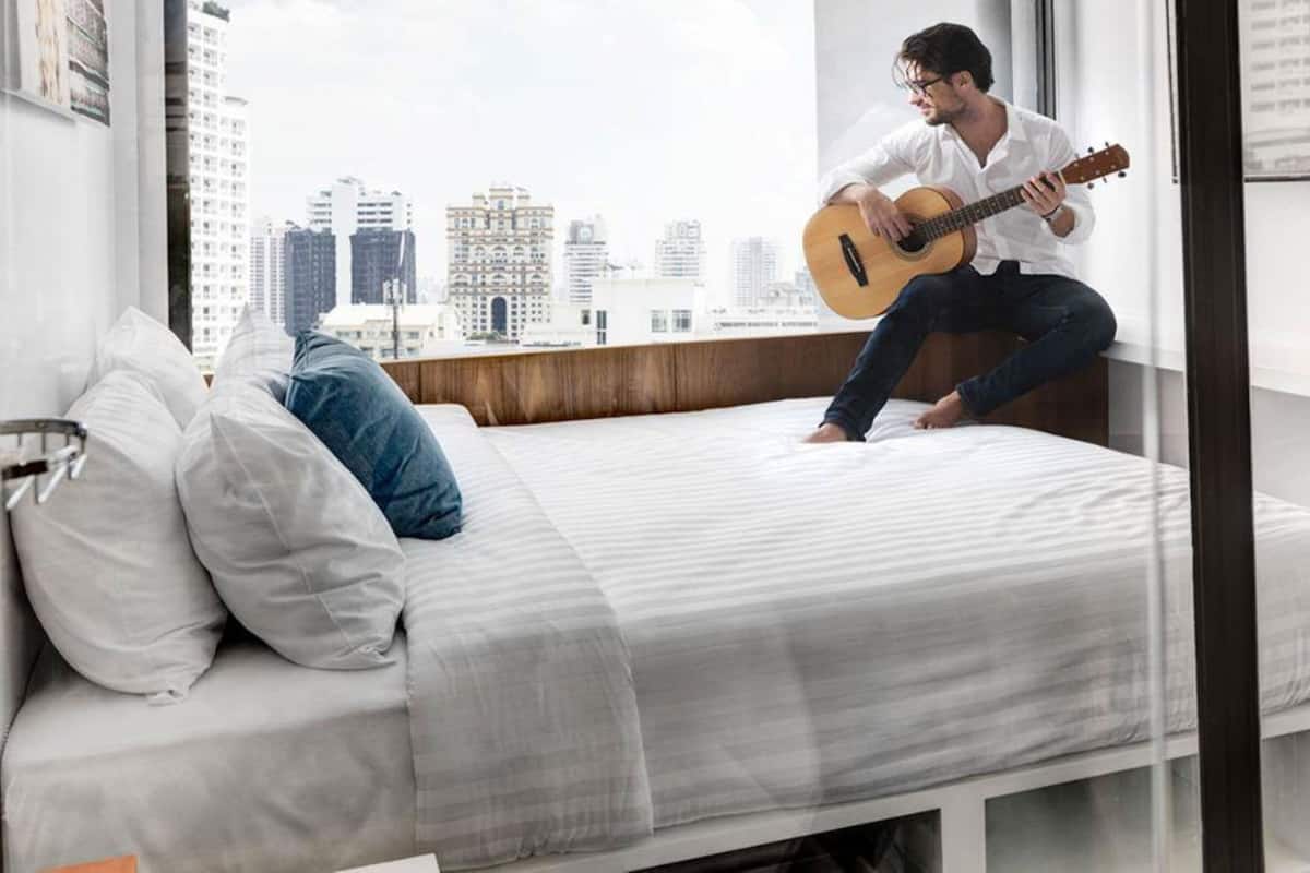 A modern bedroom with a bed, pillows, a guitar, and a city view.