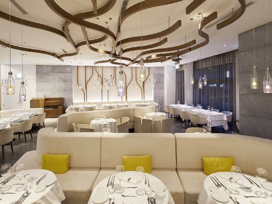 En moderne restaurant med runde borde og båse, kendetegnet ved et unikt loftsdesign og hængende lamper.