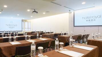 A hotel conference room with multiple tables, water bottles, and a projector screen displaying the hotel name.