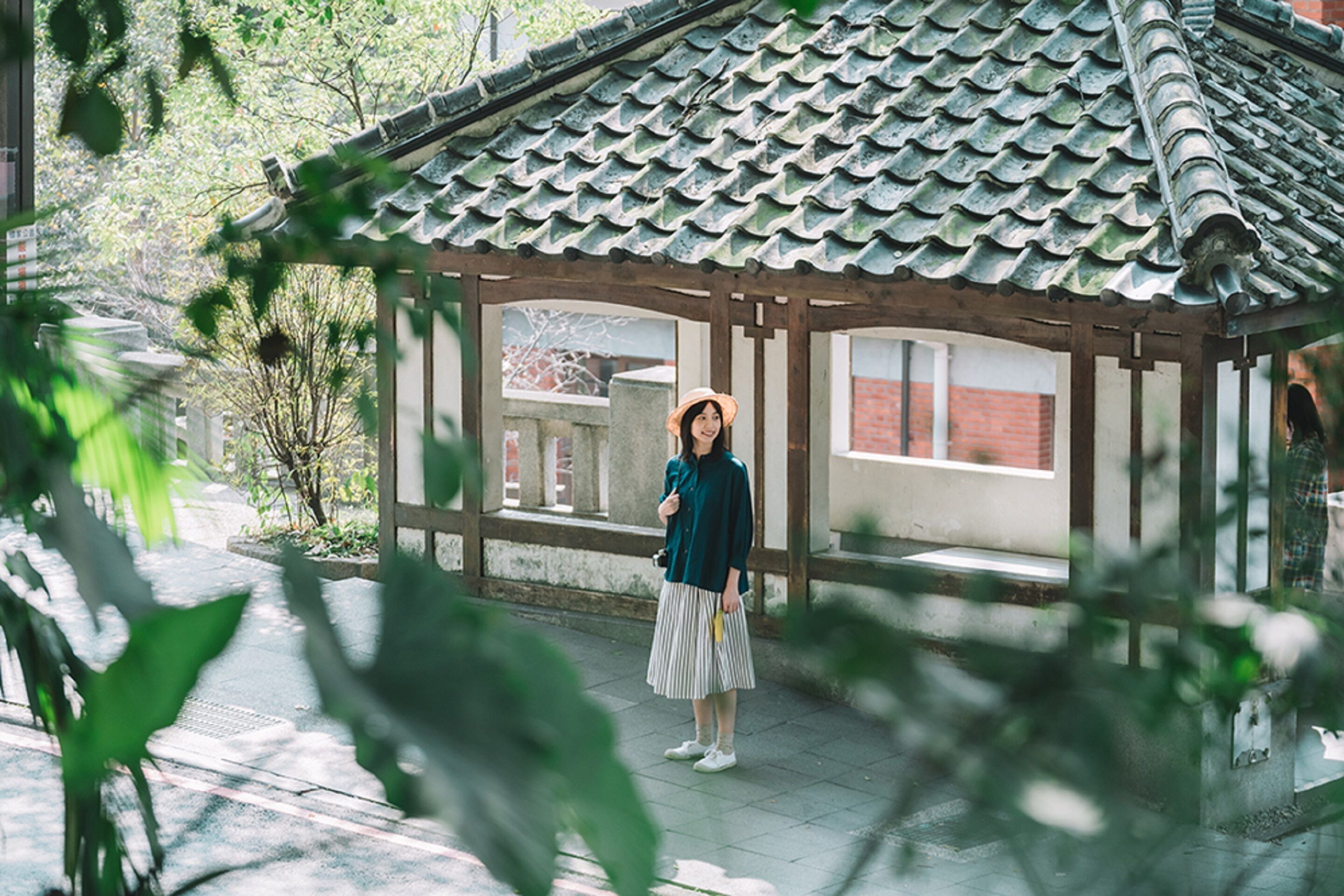 A traditional Japanese-style pavilion with a tiled roof and wooden beams, surrounded by greenery.