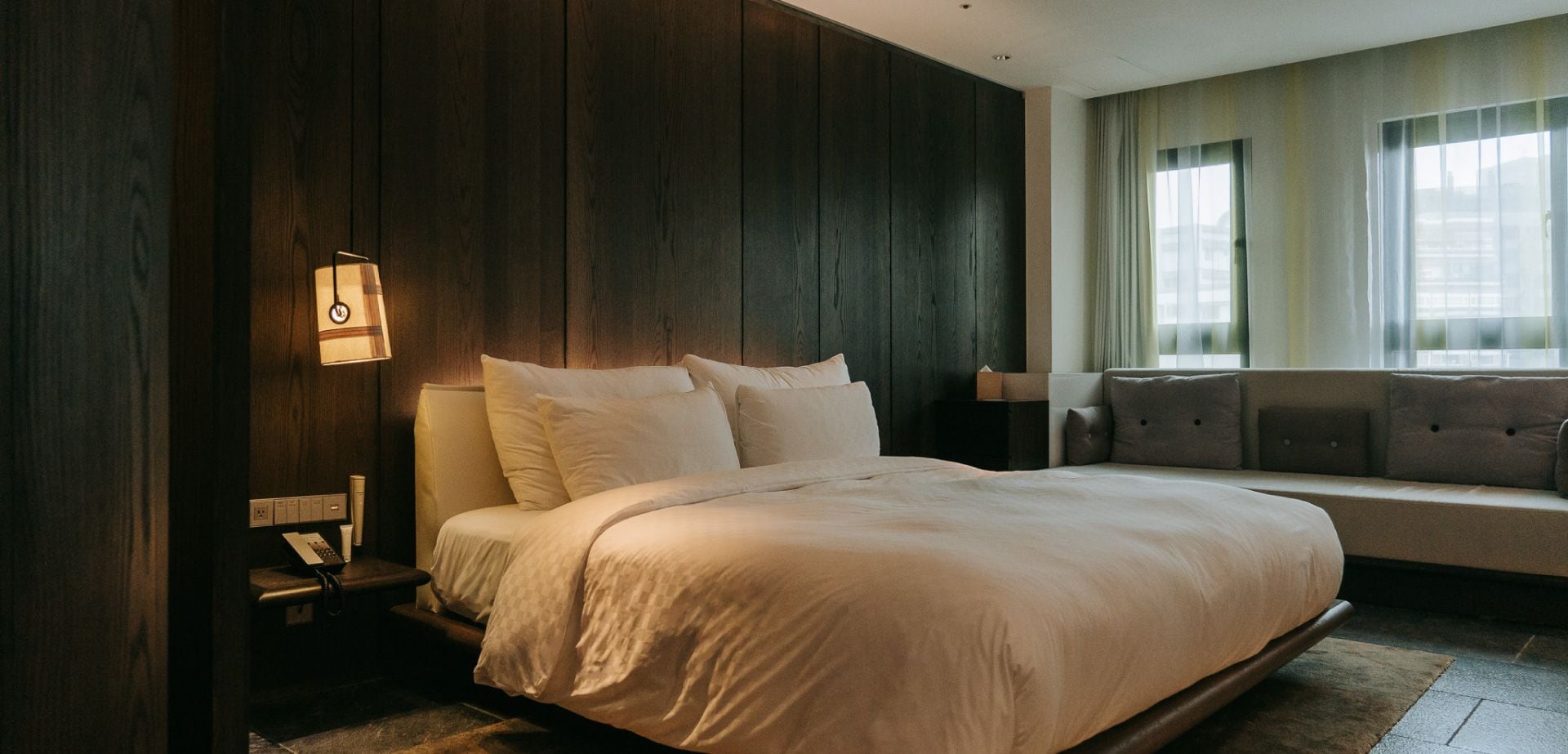 A modern hotel room with a large bed, a bedside table, and a sofa.