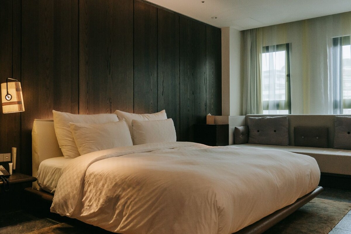 A modern hotel room with a large bed, a bedside table, and a sofa.