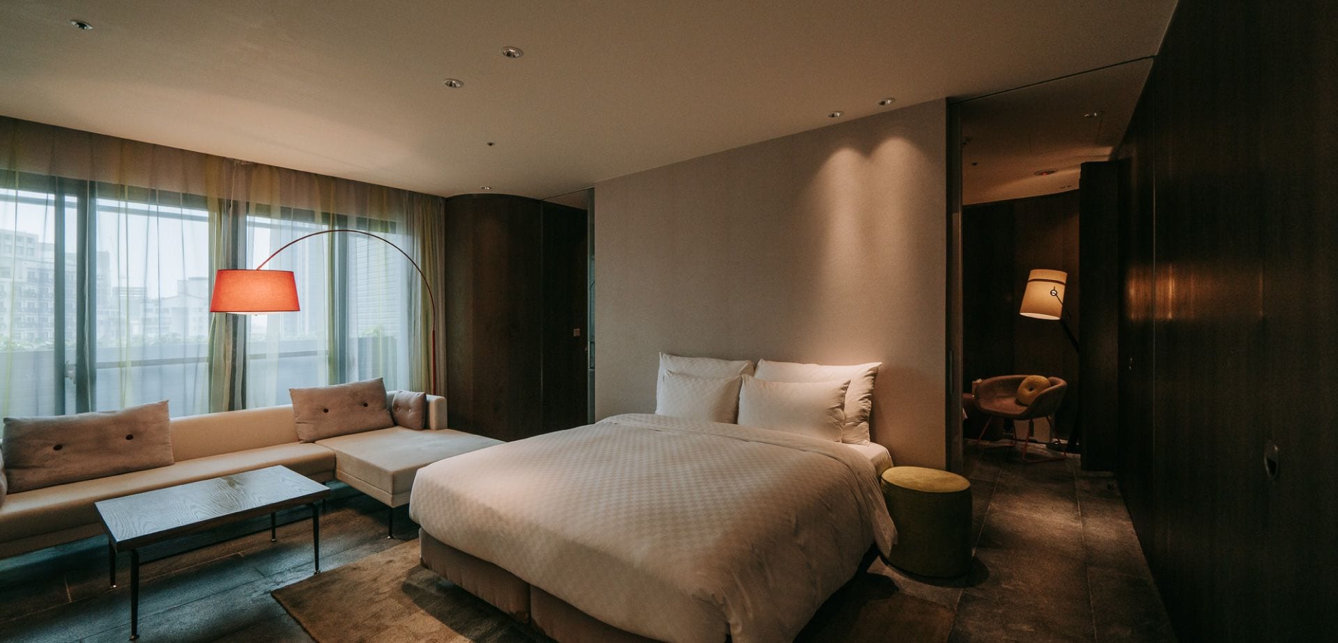 A modern hotel room with a large bed, a sofa, a small table, and a chair.