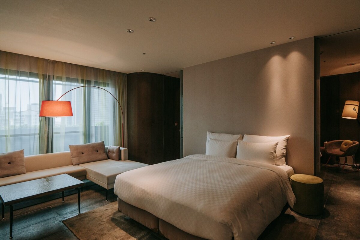 A modern hotel room with a large bed, a sofa, a small table, and a chair.