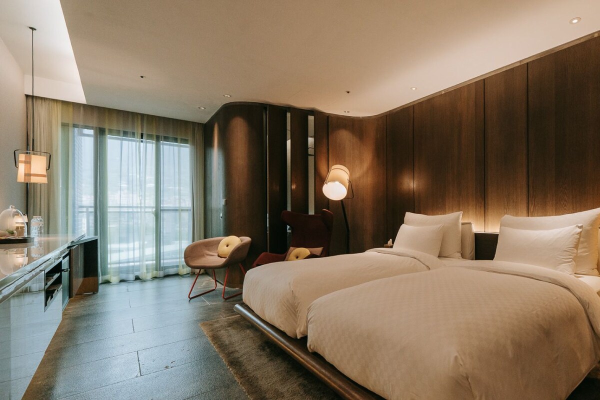 A modern hotel room with a large bed, bedside tables, a desk, and a chair.