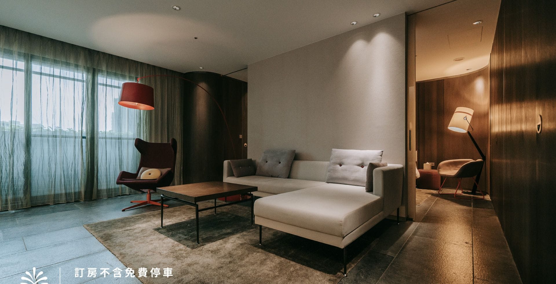 A modern hotel room with a sofa, armchair, and a dining table.