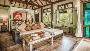 A spacious room with a large bed, a wooden coffee table, and a view of greenery through large windows. - Koh Jum Beach Villas “A member of Secret Retreats” (Nuea Khlong)