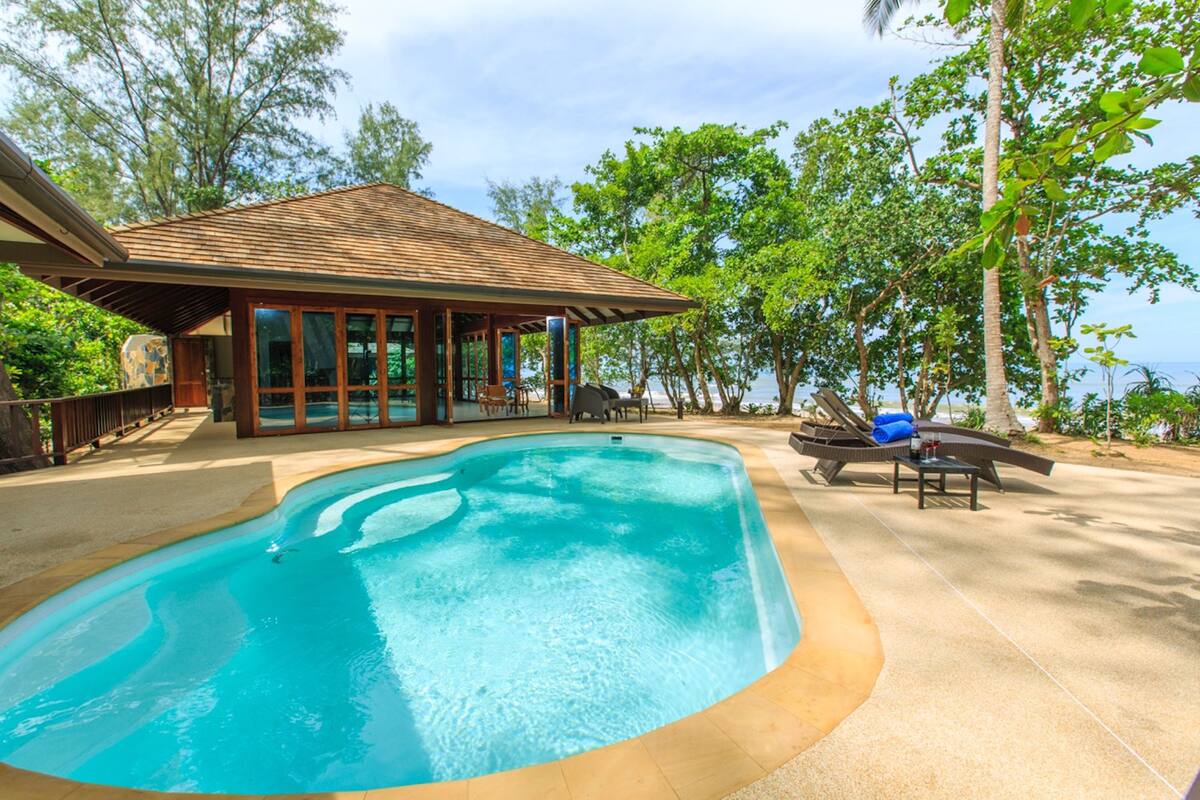 Une piscine avec une terrasse en bois, un espace salon couvert et une vue sur l’océan.