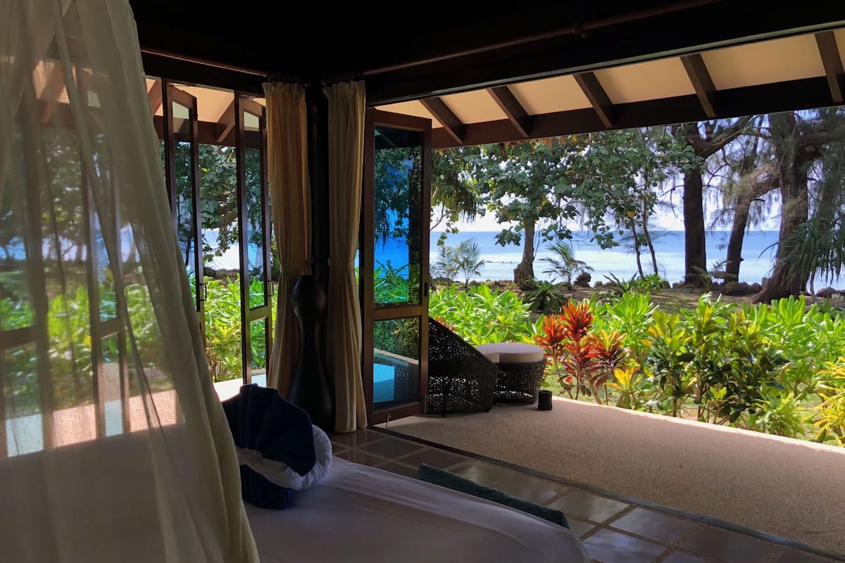 Une chambre avec un lit, une chaise et une vue sur l’océan et la verdure.
