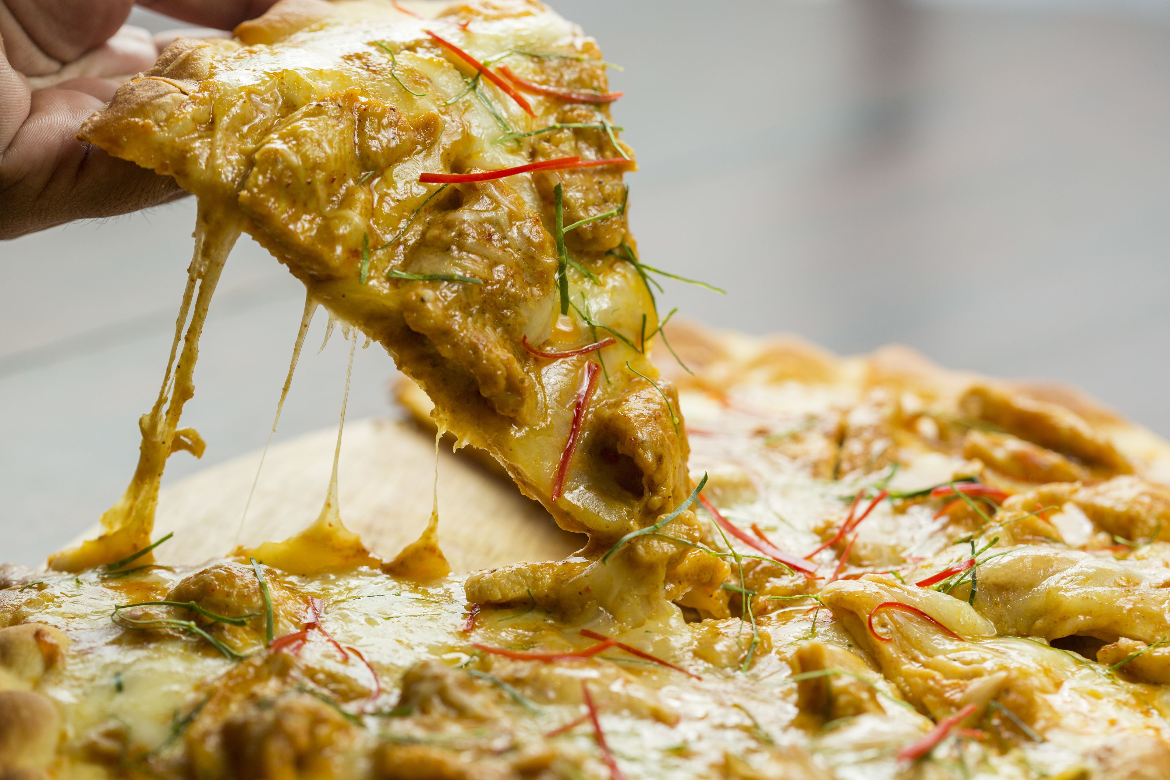 Gros plan d’une pizza dont le fromage est fondu et qui est garnie d’herbes, et que l’on soulève.
