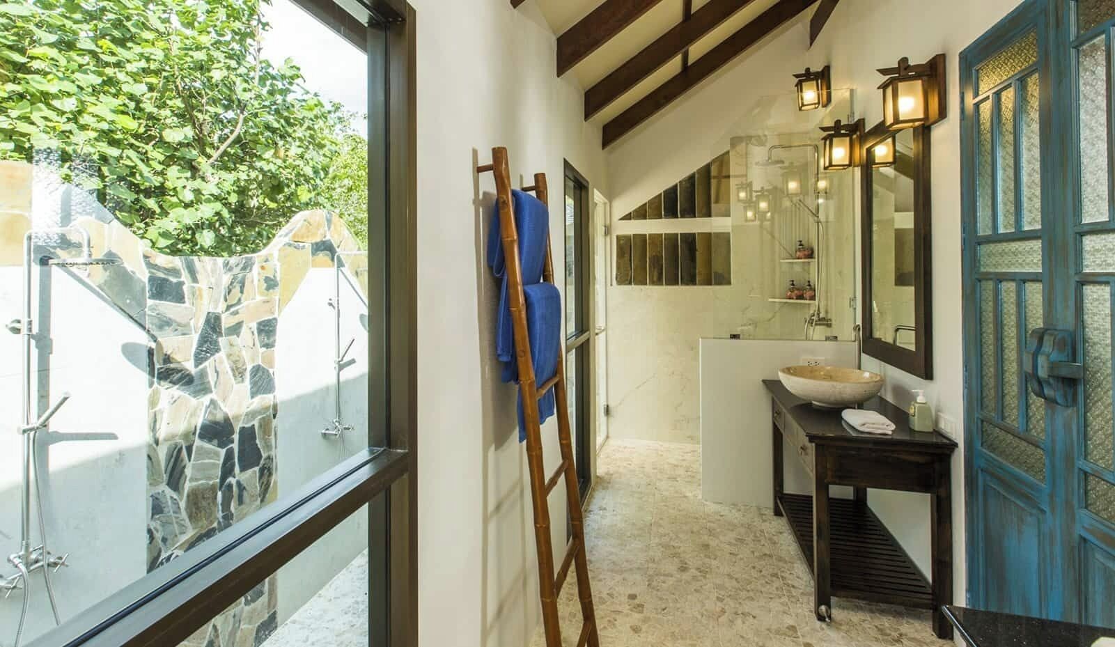 Un baño con pared de piedra, escalera de madera, lavabo con un recipiente grande y puerta azul.