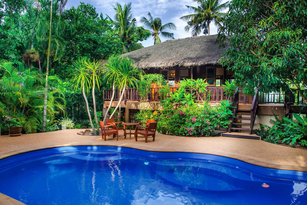 Un espace piscine agrémenté d’une structure à toit de chaume, entouré d’une végétation tropicale luxuriante.