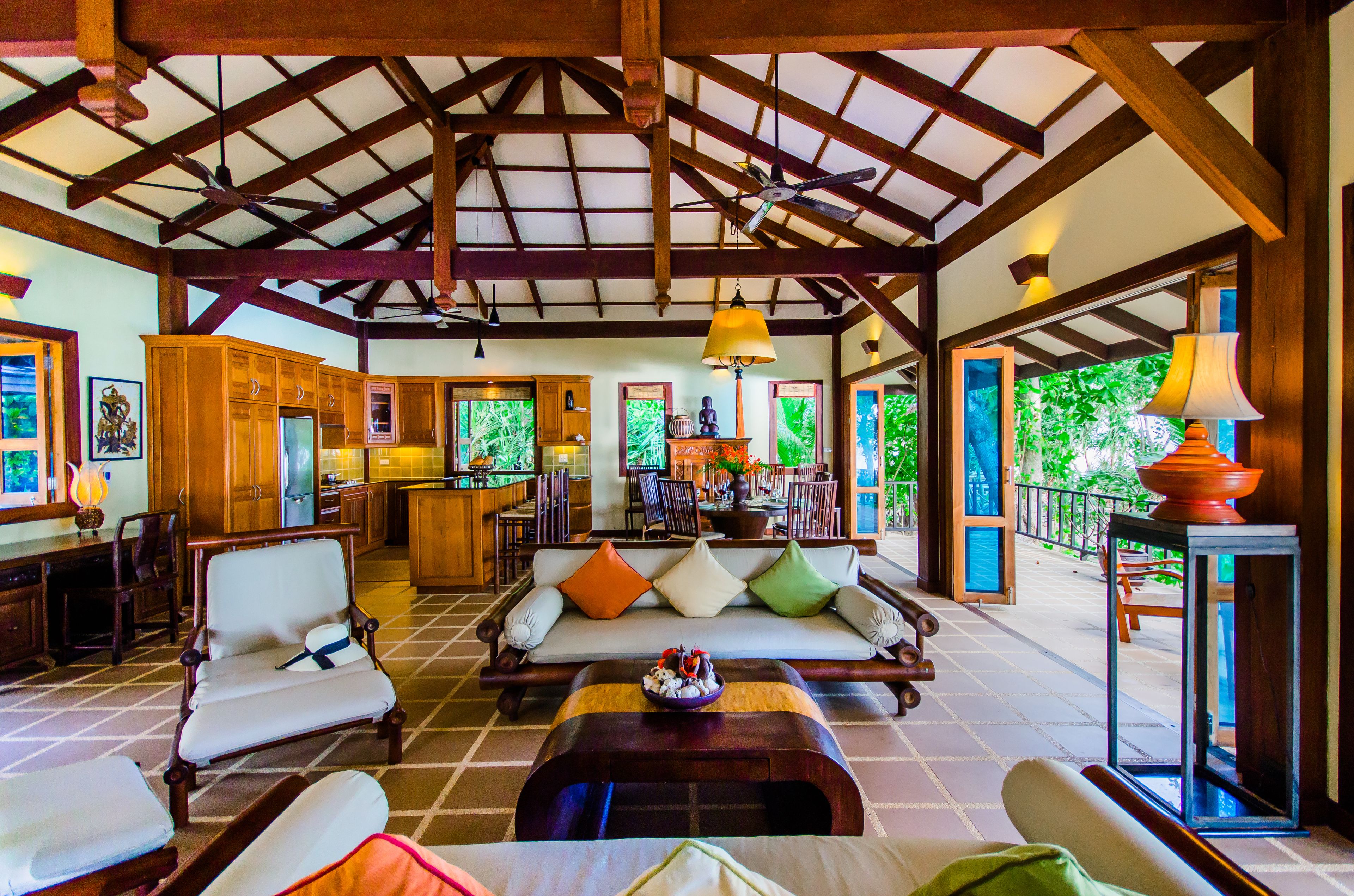 A spacious living area with a high ceiling, wooden beams, a sofa set, a dining table, and a kitchen in the background.