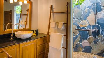 A bathroom with a stone wall, wooden cabinets, a large mirror, and a towel rack.
