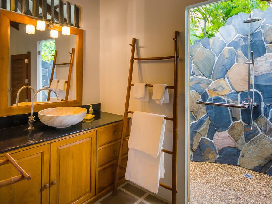 A bathroom with a stone wall, wooden cabinets, a large mirror, and a towel rack.