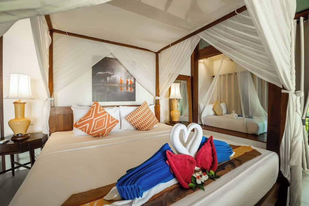 Une chambre d’hôtel avec un grand lit, un lit à baldaquin, une table de chevet avec une lampe, un miroir et un tableau au mur.