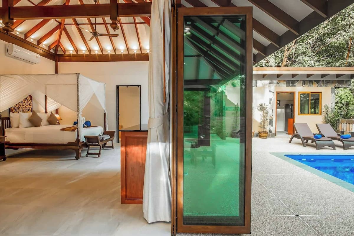 Une chambre spacieuse avec un lit, une porte vitrée donnant sur une zone avec piscine et un ventilateur de plafond.