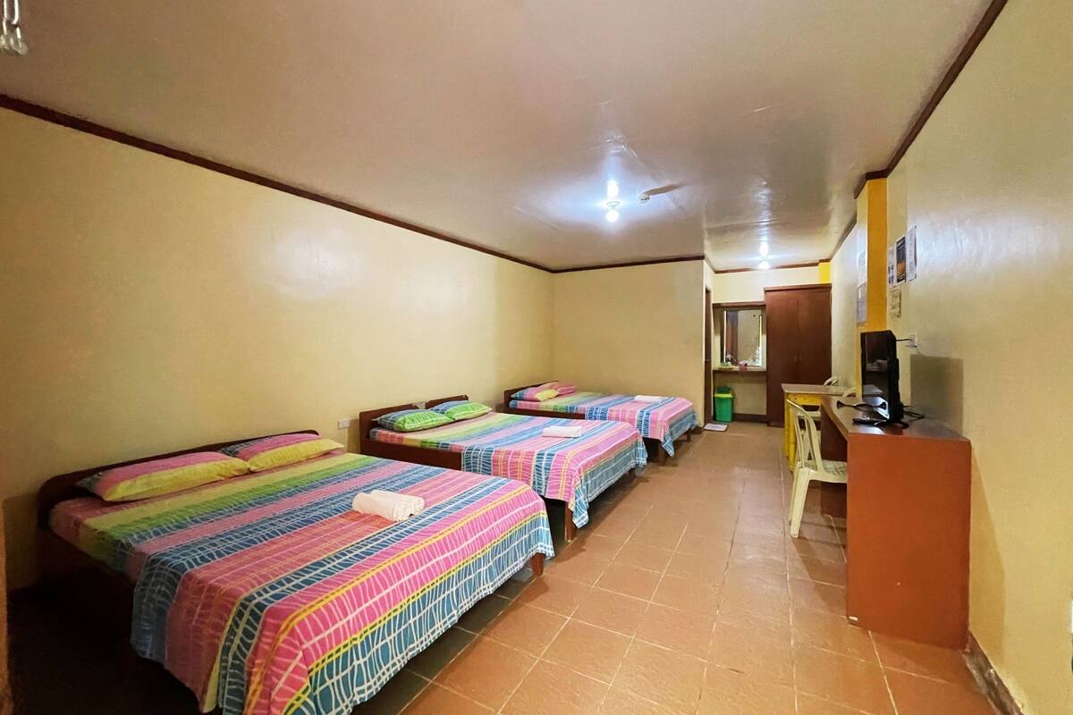 Une chambre avec quatre lits, chacun agrémenté d’une literie aux couleurs vives, d’un bureau et d’une chaise.