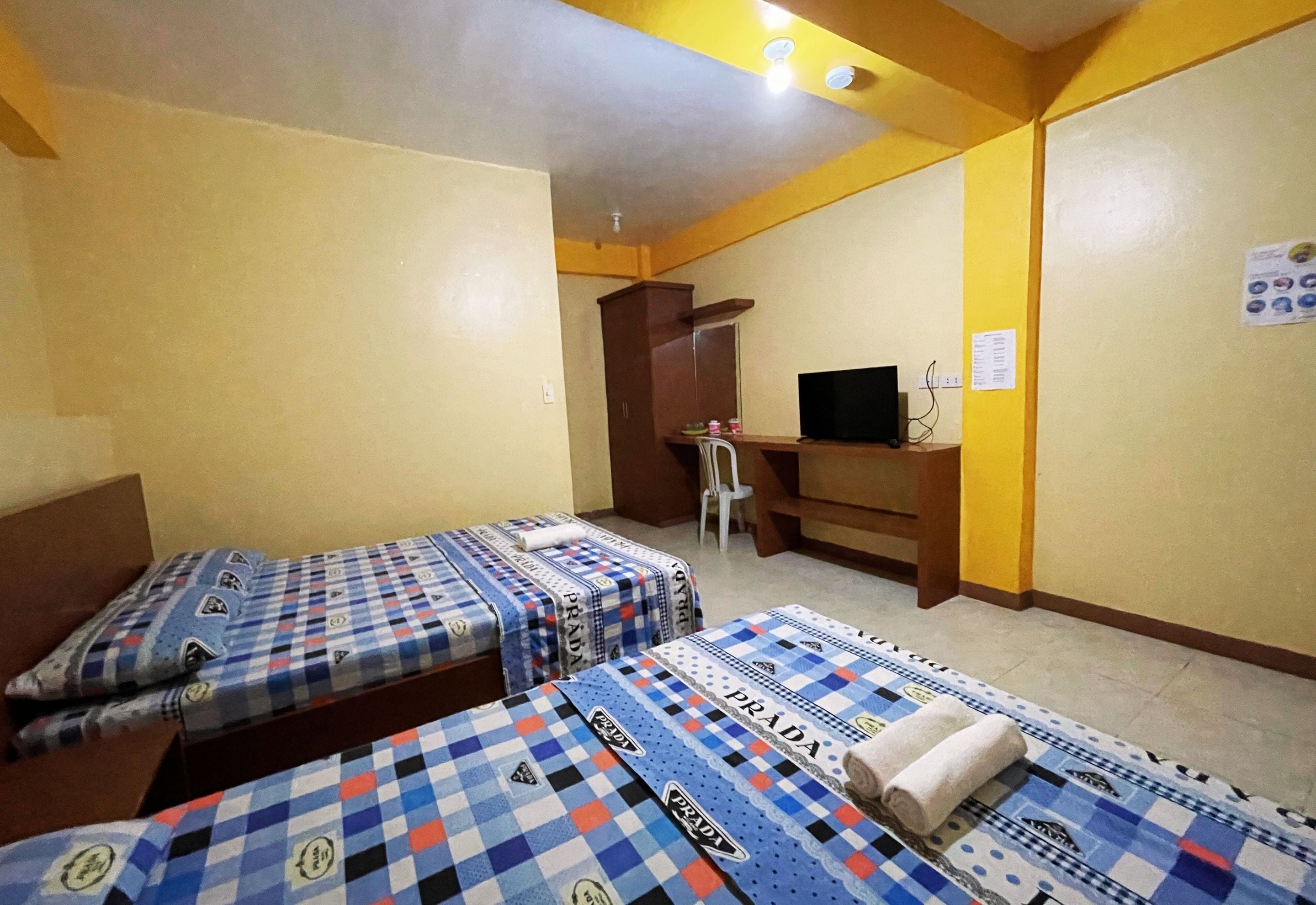 A hotel room with two beds, a desk, a chair, a television, and a wall-mounted menu board.