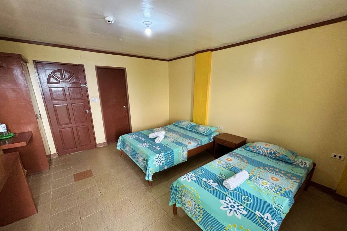 Une chambre avec deux lits simples, un bureau en bois et une porte.