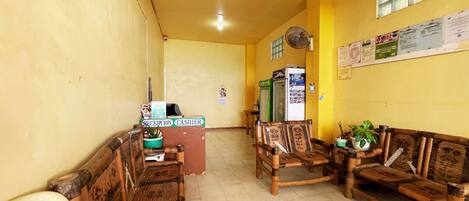 A reception area with wooden benches, a reception desk, a fan, and a bulletin board.