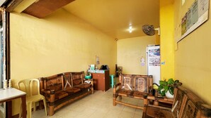A reception area with wooden benches, a reception desk, a cash register, a refrigerator, and a wall-mounted fan. - White Beach Hotel Puerto Galera powered by Cocotel (Puerto Galera)