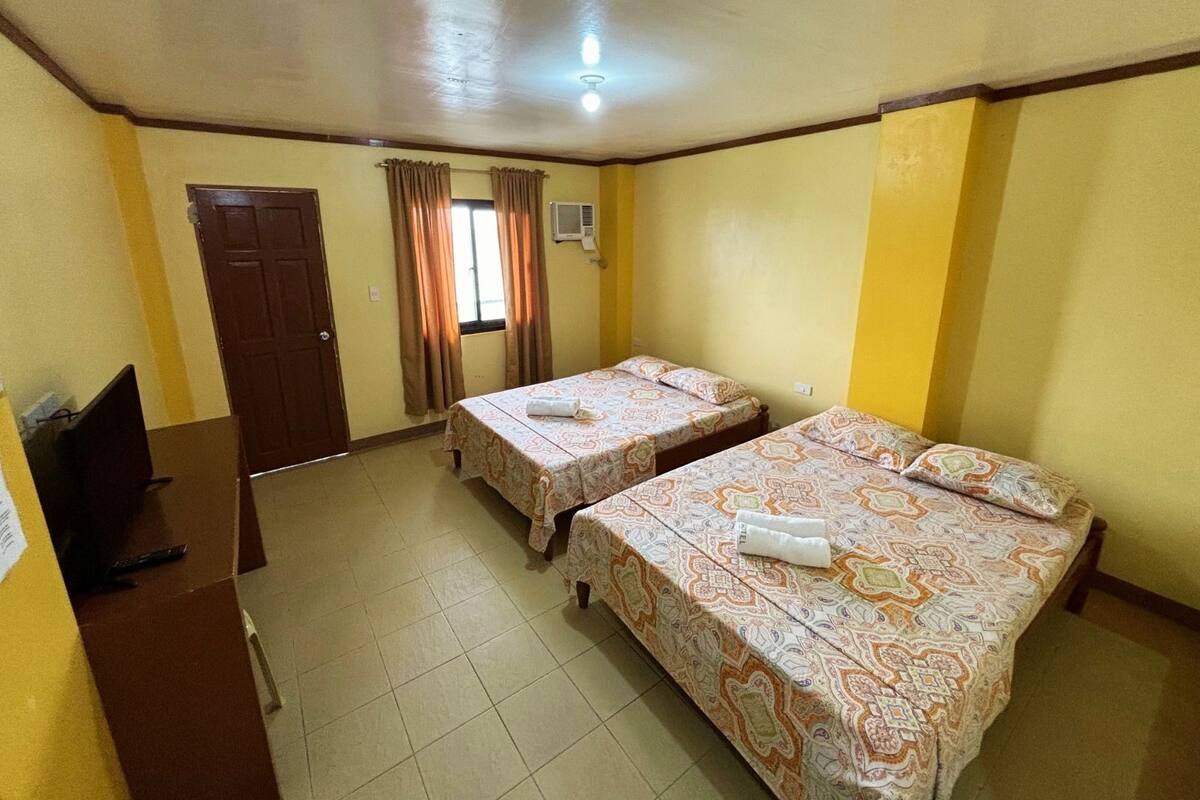 Une chambre avec deux lits, un bureau, une porte et une fenêtre avec des rideaux.