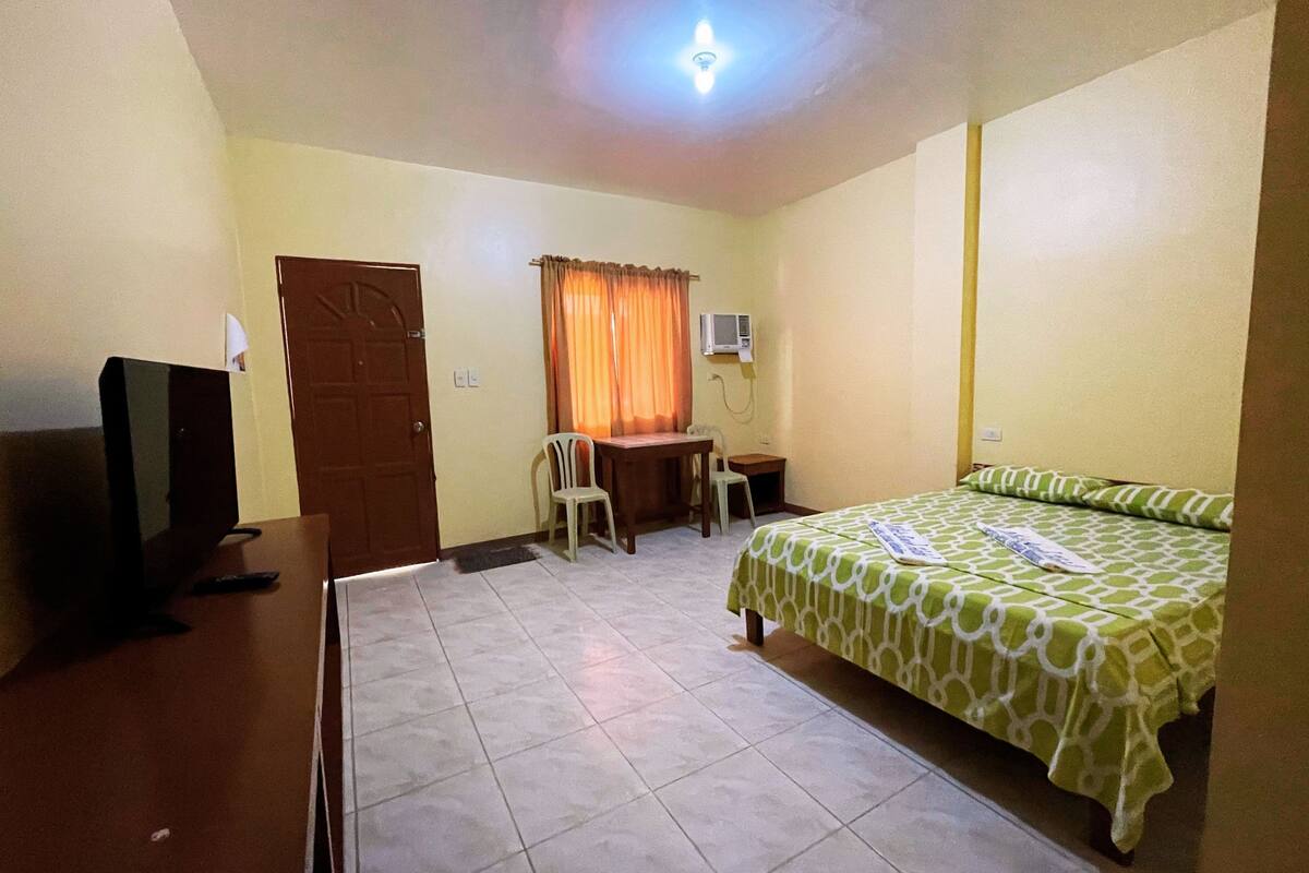 Une chambre à coucher comprenant un lit, un bureau, une chaise, un téléviseur et un appareil de climatisation.
