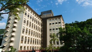 Un edificio de varios pisos con un diseño arquitectónico moderno, que presenta una combinación de ventanas rectangulares y cuadradas, y una amplia sección de vidrio en la parte superior.