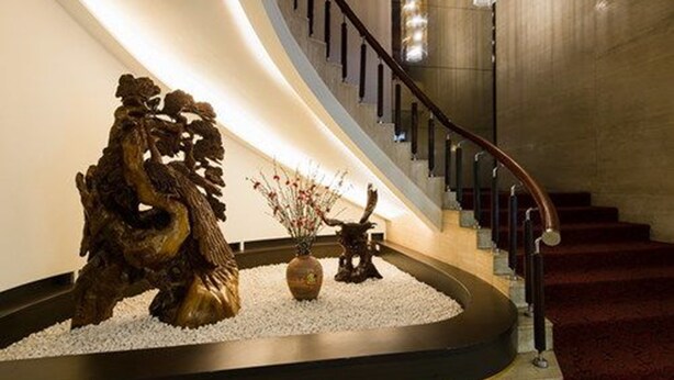 Una escalera curva con barandilla de madera, una escultura decorativa y un jarrón con flores.