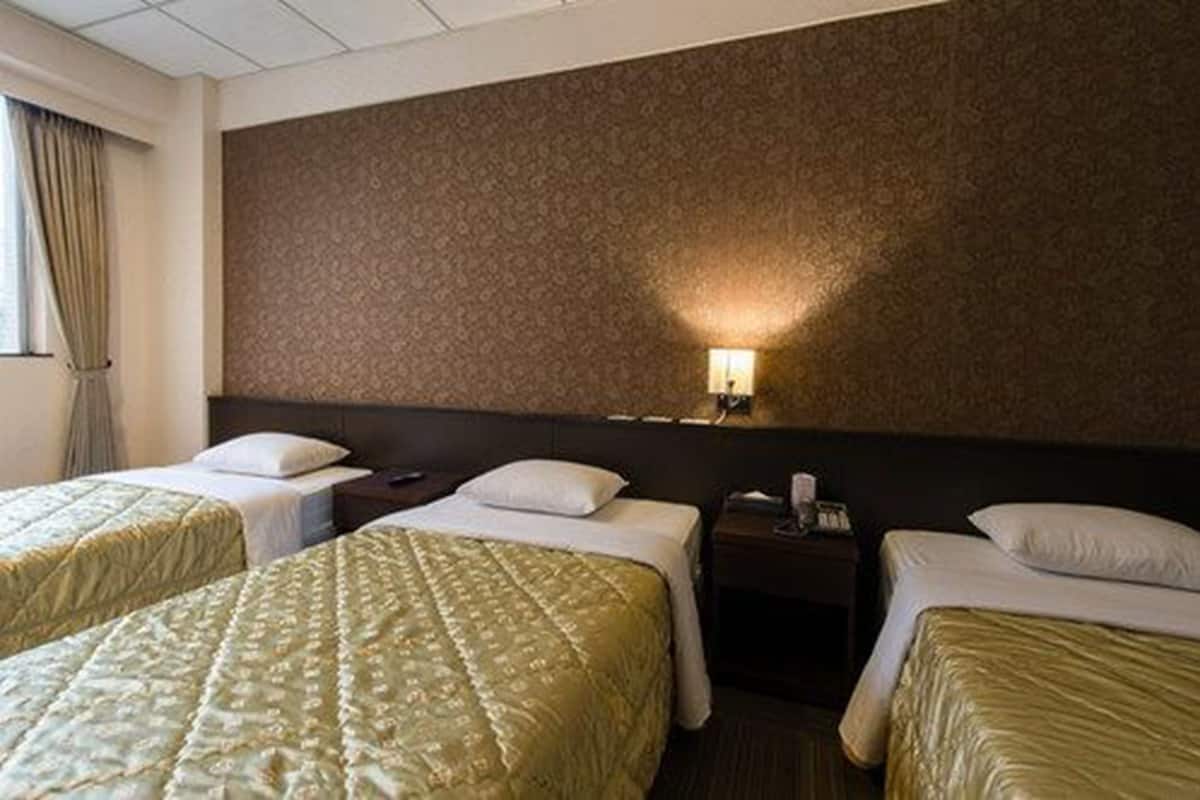 A hotel room with two beds, a nightstand, and a wall-mounted lamp.