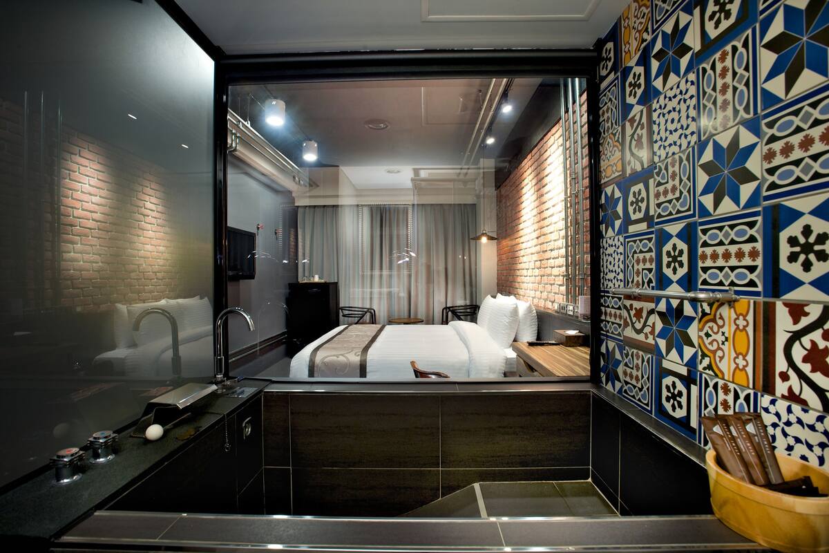 A modern hotel room with a large bed, a bathroom with a bathtub, and a decorative tile wall.