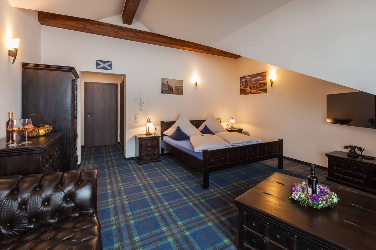 A bedroom with a bed, a dresser, a nightstand, a lamp, a television, and a plaid carpet.