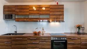 A modern kitchen with wooden cabinets, a built-in microwave, a sink, and an oven. - Vitusfort (Fuessen)