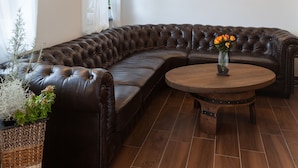 A modern living room with a leather sectional sofa, a round wooden coffee table, and a wall-mounted flat-screen TV. - Vitusfort (Fuessen)