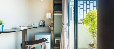 A compact room with a kitchenette, a small table, a chair, a fan, a heater, a potted plant, and a view of the outside.