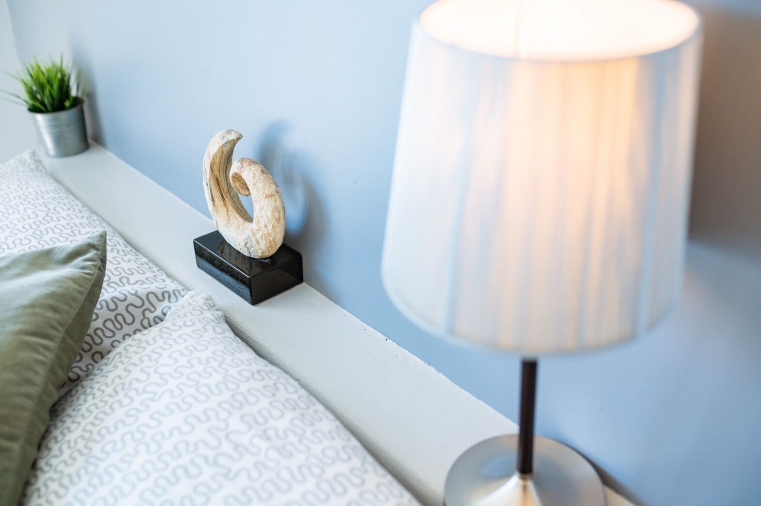 A neatly arranged bedroom with a bed, a bedside lamp, a decorative shell, and a small potted plant.