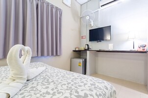 Una camera d'albergo con un letto, un piccolo frigorifero, una televisione e una scrivania con una lampada.