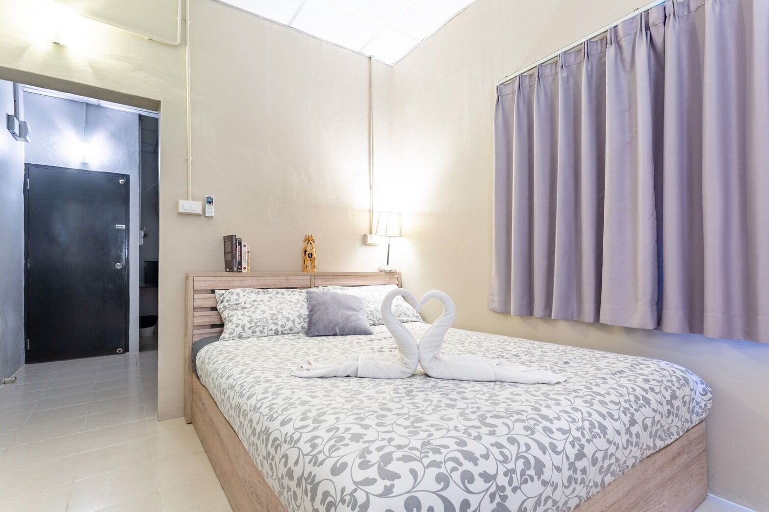 A hotel room with a bed, a nightstand, a lamp, and a door.