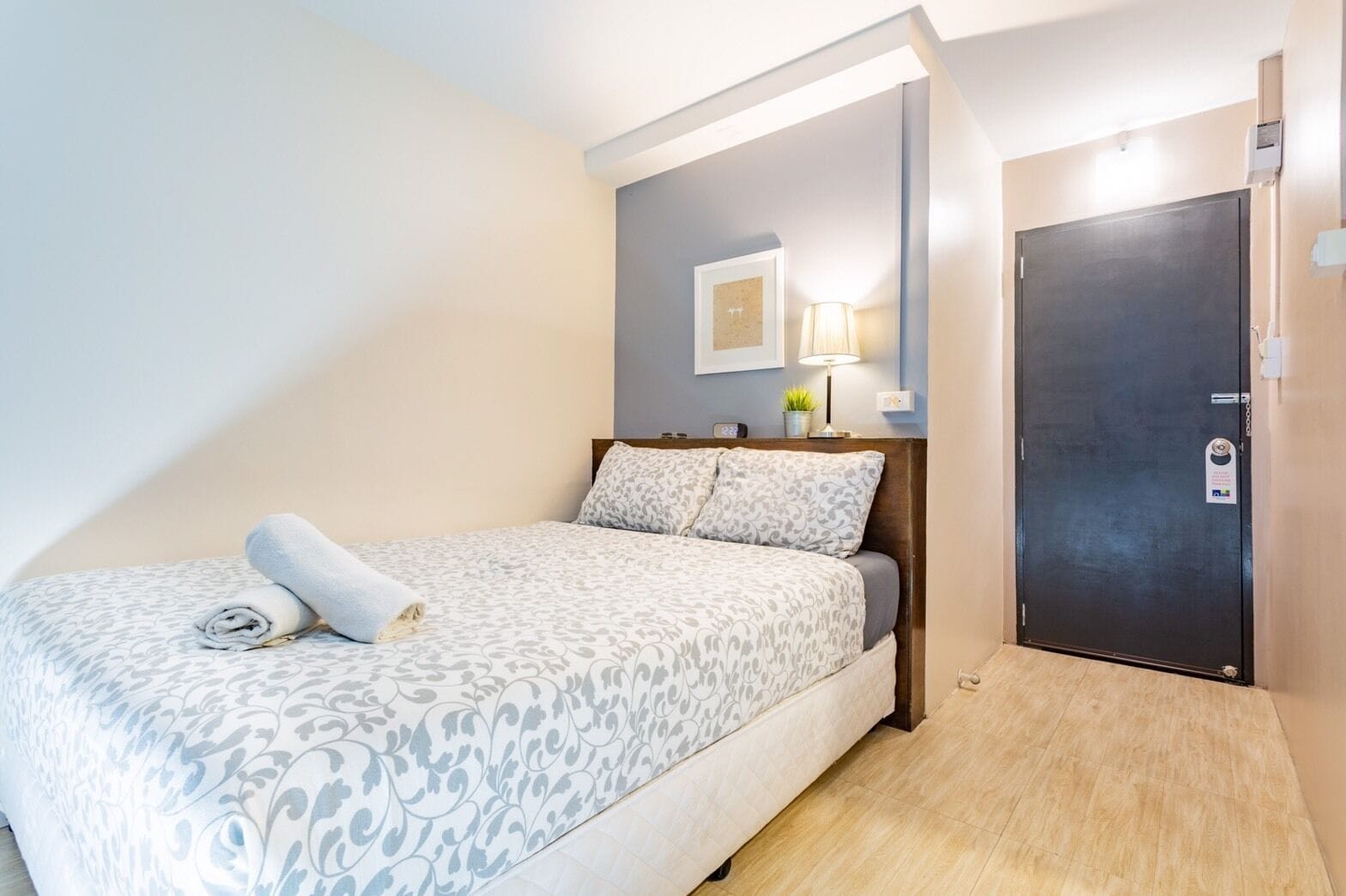 A neatly made bed with a rolled towel, a bedside lamp, and a door with a security lock.
