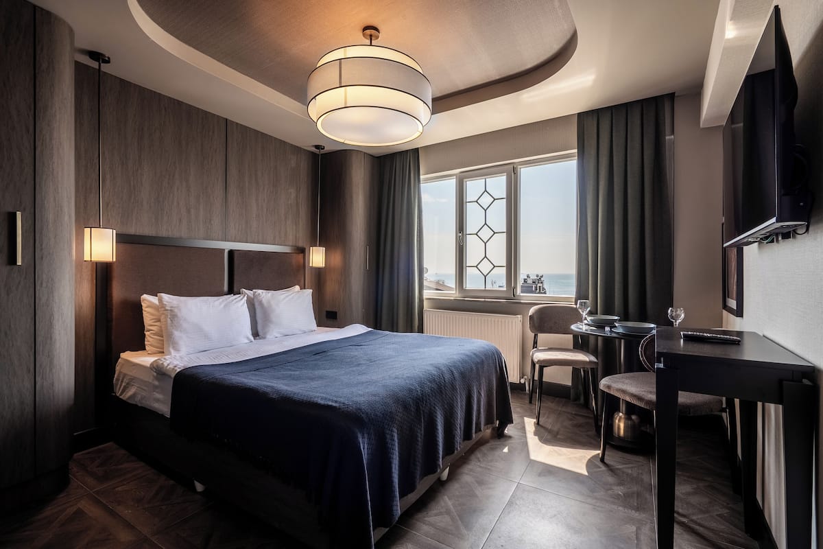 Una habitación de hotel moderna con una cama grande, un escritorio, una silla, un televisor y una ventana con vista a la ciudad.