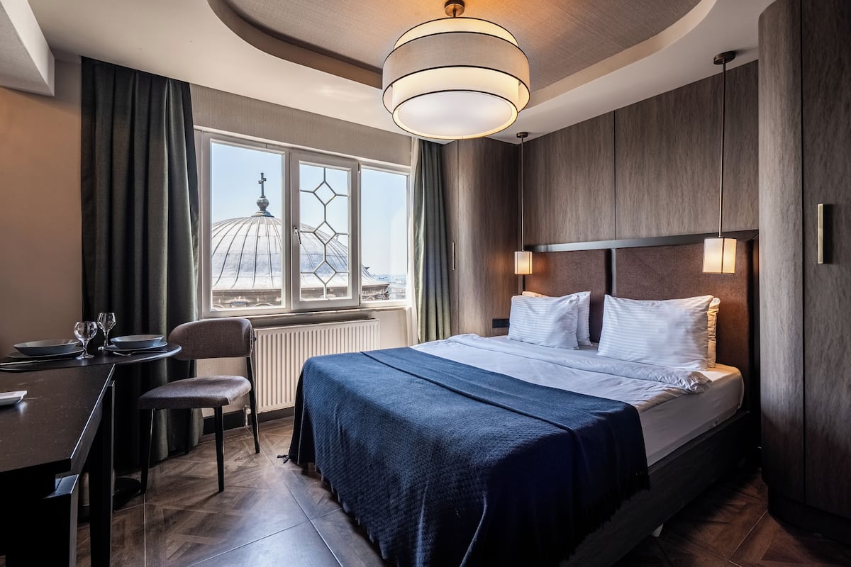 Habitación de hotel con cama, escritorio y sillas, vista a una estructura en forma de cúpula y un moderno candelabro.